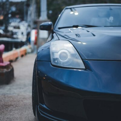 A sleek black sports car is parked on a harbor pathway, showcasing its stylish design.