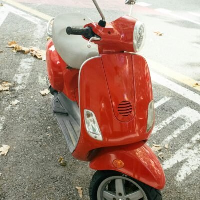 A bright red scooter parked on a street with fallen leaves, showcasing urban lifestyle.